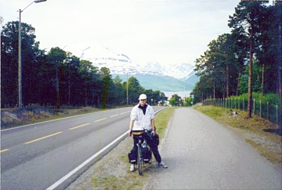 A picture of me on a bicycle, with a Norwegian fjord and some mountains in the background.